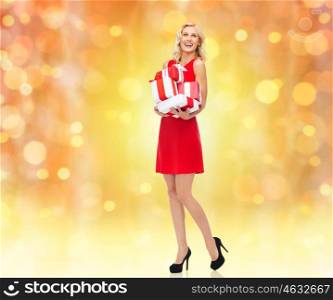 people, christmas, birthday and holidays concept - happy young woman in red dress holding gift boxes over lights background