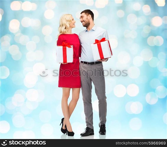 people, christmas, birthday, couple and holidays concept - happy young man and woman with gift boxes over blue lights background