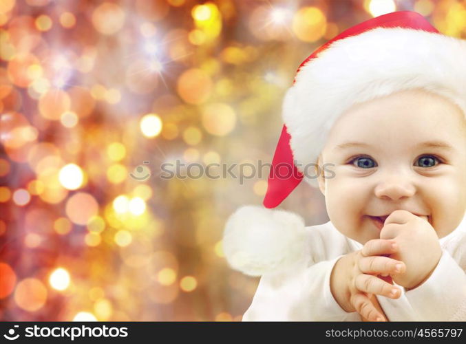 people, christmas, children and holidays concept - happy baby in santa hat over lights background