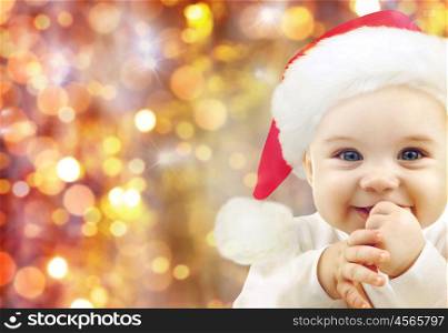 people, christmas, children and holidays concept - happy baby in santa hat over lights background
