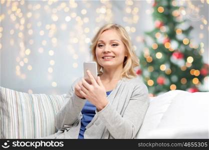people, christmas, communication, technology and internet concept - smiling woman with smartphone texting at home over holidays lights background