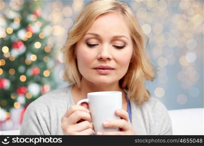 people, christmas, guesswork, drinks and leisure concept - woman with cup of tea or coffee at home over holidays lights background