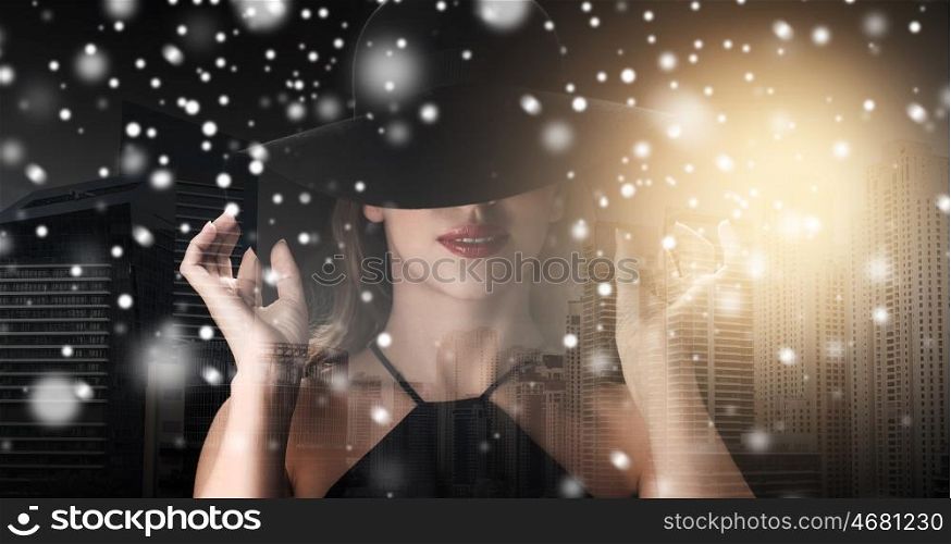people, christmas, holidays and fashion concept - beautiful woman in black hat over dark over dubai city background with snow, double exposure and highlight