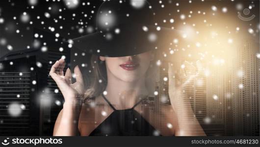 people, christmas, holidays and fashion concept - beautiful woman in black hat over dark over dubai city background with snow, double exposure and highlight
