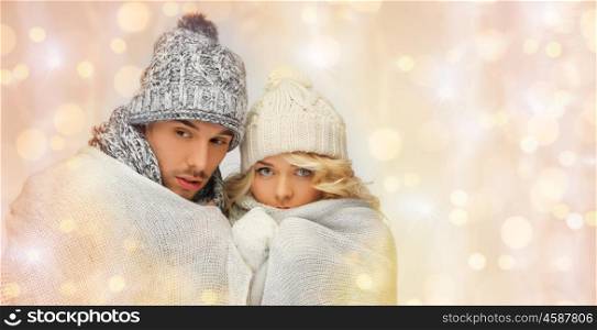 people, christmas, holidays and new year concept - freezing couple in winter clothes wrapped in plaid over holidays lights background