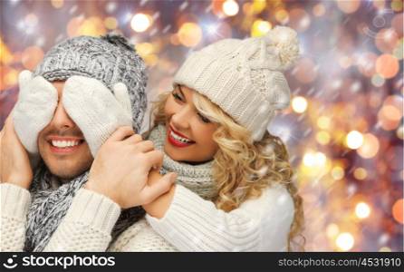people, christmas, holidays and new year concept - happy family couple in winter clothes playing guess who game over holidays lights and snow background