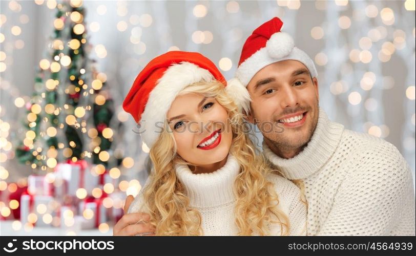 people, christmas, holidays and new year concept - happy family couple in sweaters and santa hats over lights background