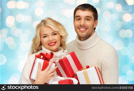people, christmas, holidays and new year concept - happy family couple in sweaters holding gifts or presents over blue lights background