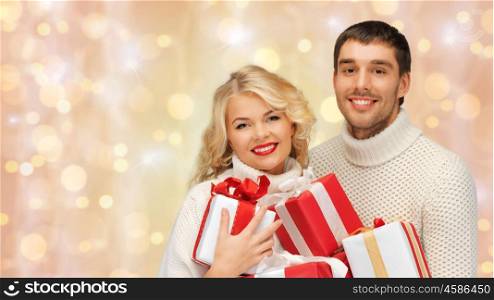 people, christmas, holidays and new year concept - happy family couple in sweaters holding gifts or presents over holidays lights and snow background