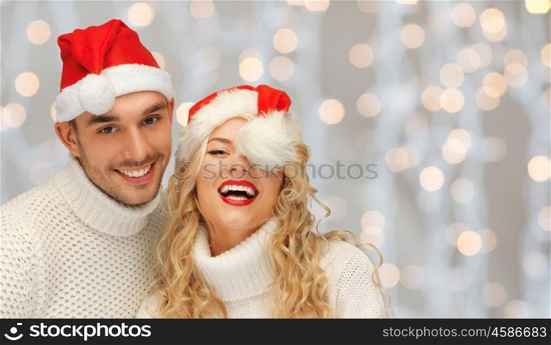 people, christmas, holidays and new year concept - happy family couple in sweaters and santa hats over lights background
