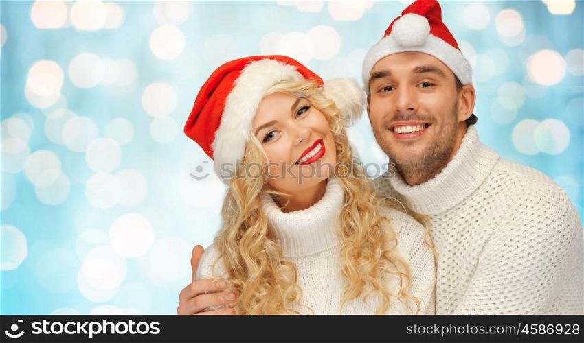 people, christmas, holidays and new year concept - happy family couple in sweaters and santa hats over blue blue lights background