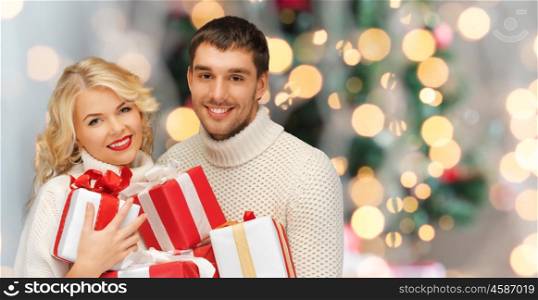 people, christmas, holidays and new year concept - happy family couple in sweaters holding gifts or presents over lights background