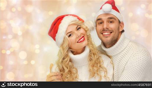 people, christmas, holidays and new year concept - happy family couple in sweaters and santa hats hugging over holidays lights and snow background