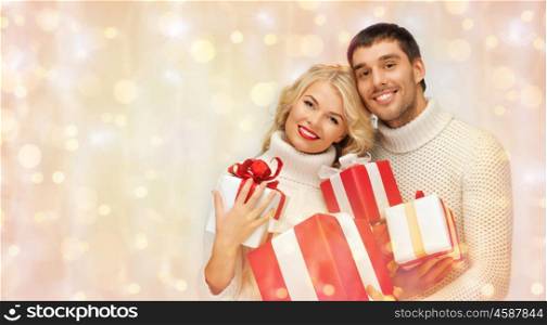 people, christmas, holidays and new year concept - happy family couple in sweaters holding gifts or presents over holidays lights and snow background