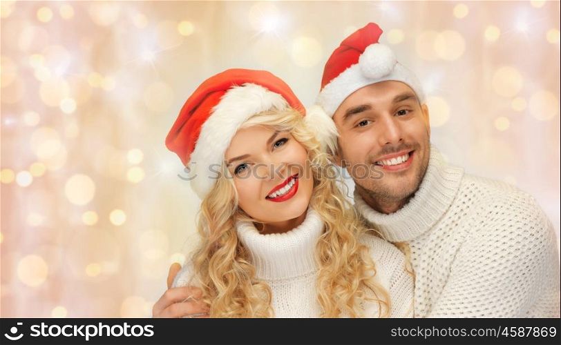 people, christmas, holidays and new year concept - happy family couple in sweaters and santa hats hugging over holidays lights and snow background