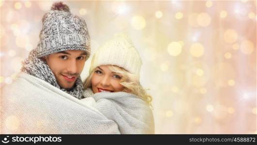 people, christmas, holidays and new year concept - happy family couple in winter clothes wrapped in plaid over holidays lights background