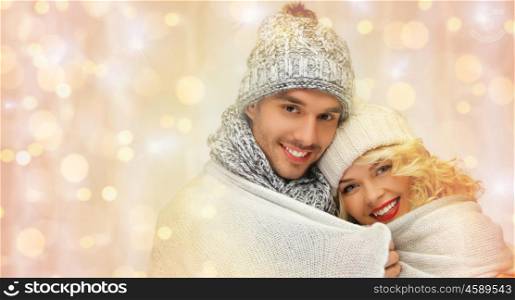 people, christmas, holidays and new year concept - happy family couple in winter clothes wrapped in plaid over holidays lights background