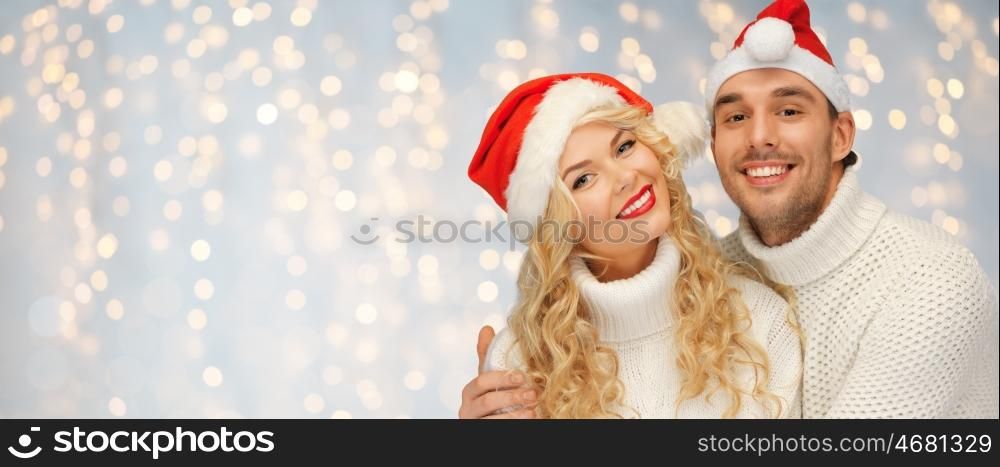 people, christmas, holidays and new year concept - happy family couple in sweaters and santa hats over holidays lights background