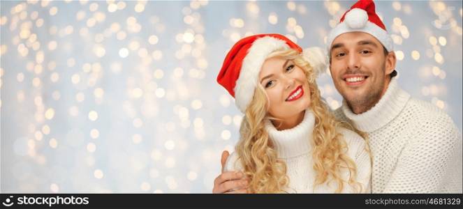 people, christmas, holidays and new year concept - happy family couple in sweaters and santa hats over holidays lights background