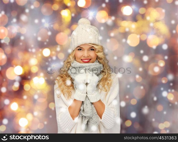 people, christmas, holidays and new year concept - happy smiling beautiful woman in winter hat, scarf and mittens over holidays lights and snow background