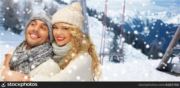 people, christmas, holidays and season concept - happy family couple in winter clothes hugging over wooden swing and snowy mountains background