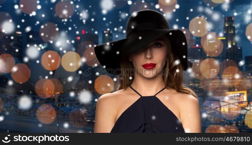people, christmas, holidays, luxury and fashion concept - beautiful woman in black hat over night singapore city lights background and snow