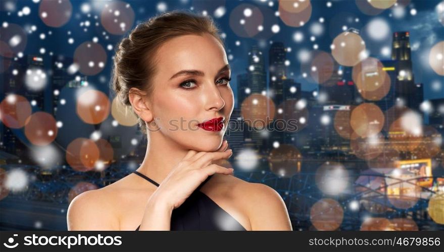 people, christmas, holidays, luxury and fashion concept - beautiful woman in black with red lips over night singapore city lights background and snow