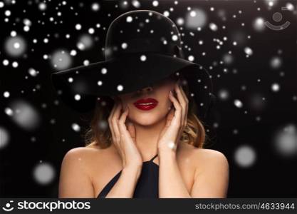 people, christmas, holidays, luxury and fashion concept - beautiful woman in hat over black background and snow. beautiful woman in black hat over snow