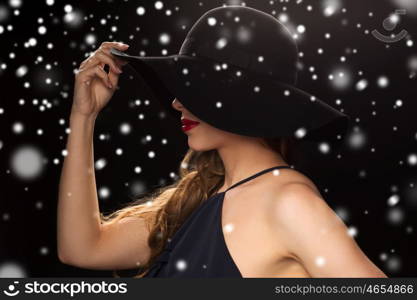 people, christmas, holidays, luxury and fashion concept - beautiful woman in hat over black background and snow