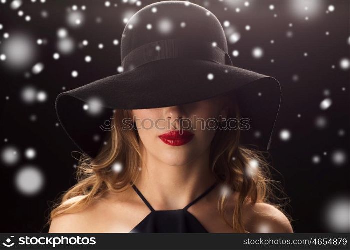 people, christmas, holidays, luxury and fashion concept - beautiful woman in hat over black background and snow