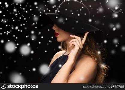 people, christmas, holidays, luxury and fashion concept - beautiful woman in hat over black background and snow