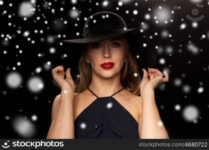 people, christmas, holidays, luxury and fashion concept - beautiful woman in hat over black background and snow