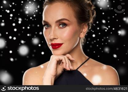 people, christmas, holidays, luxury and fashion concept - close up of beautiful woman with red lips over black background and snow