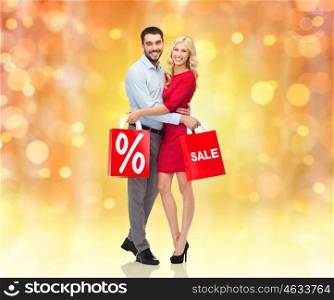people, christmas, sale, discount and holidays concept - happy couple hugging with red shopping bags over lights background