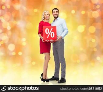 people, christmas, sale, discount and holidays concept - happy couple with red sale sign over lights background. happy couple with red sale sign