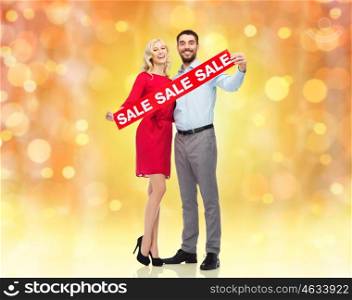 people, christmas, sale, discount and holidays concept - happy couple with red sale sign over lights background