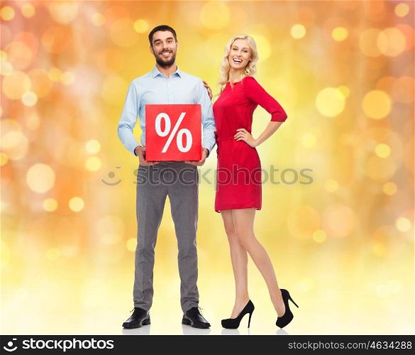 people, christmas, sale, discount and holidays concept - happy couple with red sale sign over lights background
