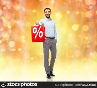 people, christmas, sale, discount and holidays concept - smiling man holding red shopping bags with percentage sign over lights background