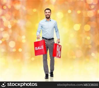 people, christmas, sale, discount and holidays concept - smiling man holding red shopping bags with percentage sign over lights background