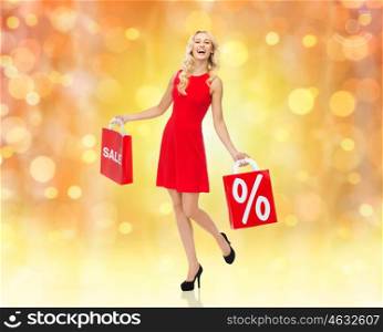people, christmas, sale, discount and holidays concept - smiling woman in red dress with shopping bags over lights background