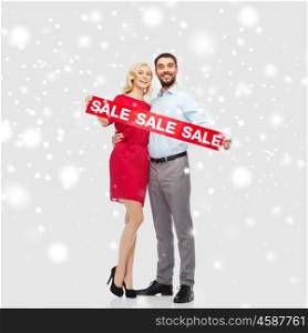 people, christmas, shopping, winter and holidays concept - happy couple with red sale sign over snow background