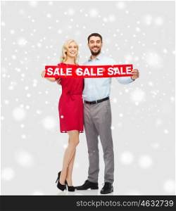 people, christmas, shopping, winter and holidays concept - happy couple with red sale sign over snow background