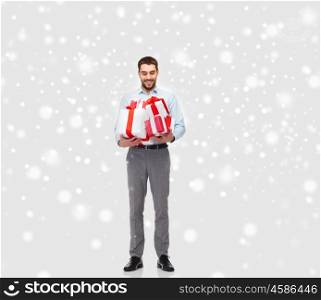 people, christmas, winter and holidays concept - happy young man holding gift boxes over snow background