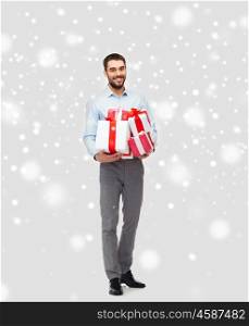 people, christmas, winter and holidays concept - happy young man holding gift boxes over snow background