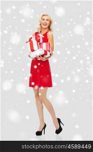 people, christmas, winter and holidays concept - happy young woman in red dress holding gift boxes over snow background