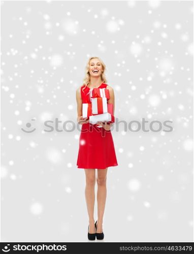 people, christmas, winter and holidays concept - happy young woman in red dress holding gift boxes over snow background