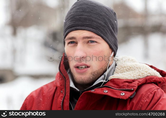 people, christmas, winter and season concept - close up of man in jacket and hat with earphones listening to music outdoors