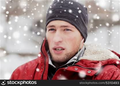 people, christmas, winter and season concept - close up of man in jacket and hat with earphones listening to music outdoors. man with earphones listening to music in winter