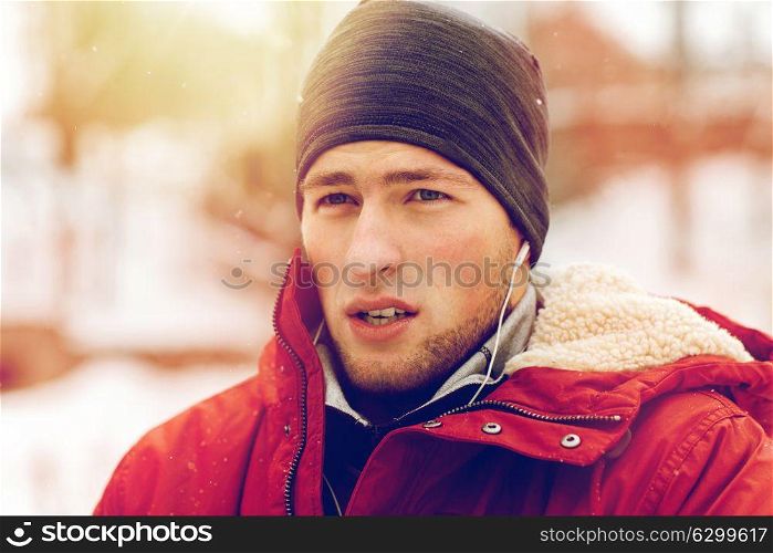 people, christmas, winter and season concept - close up of man in jacket and hat with earphones listening to music outdoors. man with earphones listening to music in winter