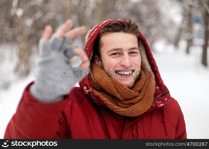 people, christmas, winter and season concept - happy smiling man in hood and scarf outdoors showing ok hand sign